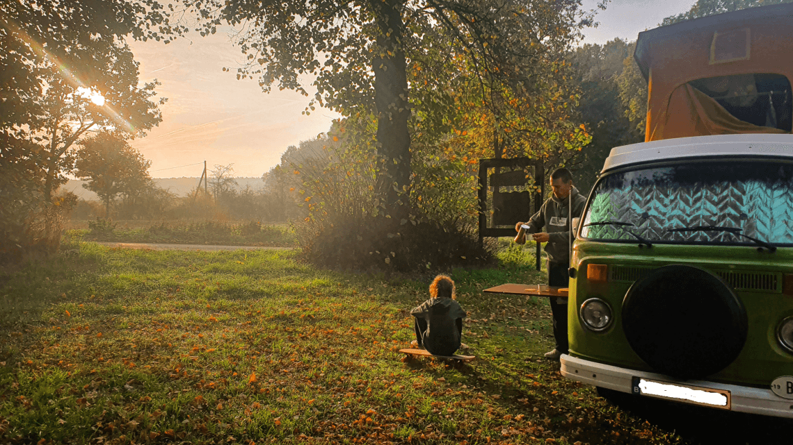 Frau vor Bulli auf Stellplatz im Sonnenuntergang im grünen 